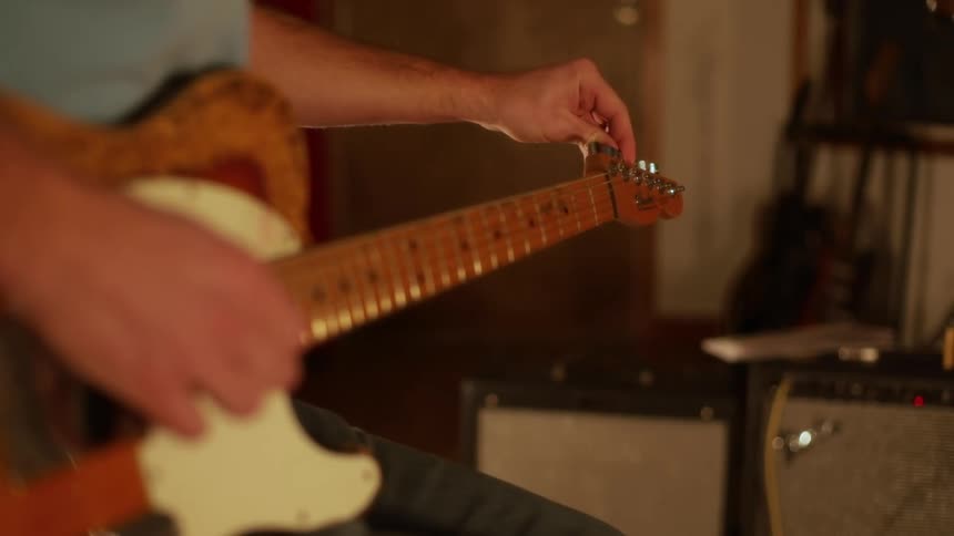 A musician adjusts the tuning pegs of an electric guitar the warm indoor lighting highlighting the wood grain and nearby amplifier