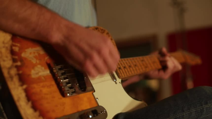 A close view of a person playing a sunburst electric guitar with a worn body and a light wood neck in a room with a red wall