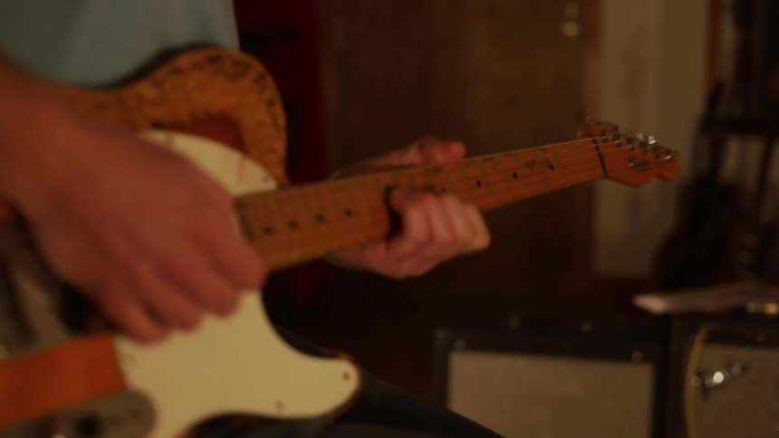A man is seated and prepares to begin playing his electric guitar