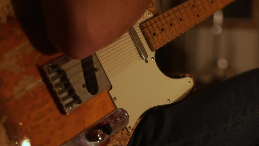 Adult man sitting down indoors and playing an electric guitar