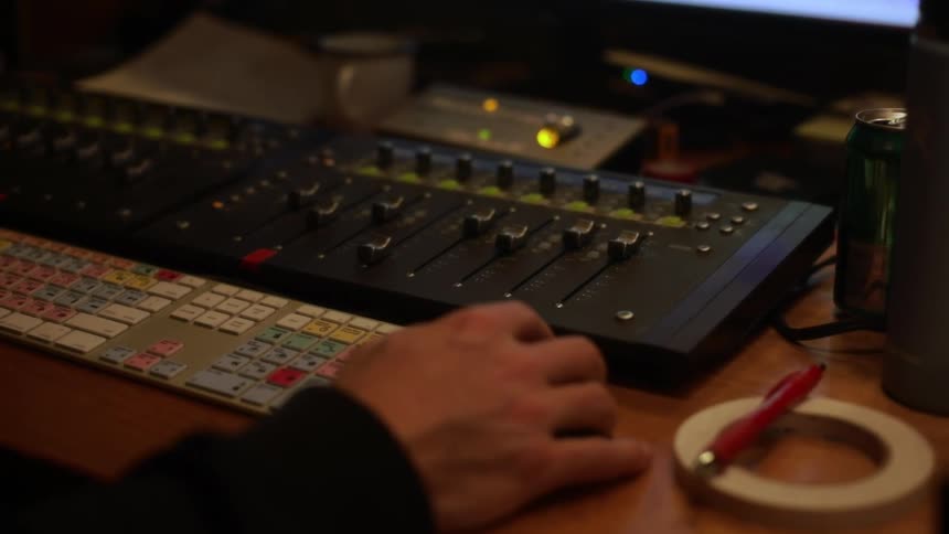 Human adult male hand tapping on a wooden desk next to a computer keyboard and a mixer in front of a computer screen indoors