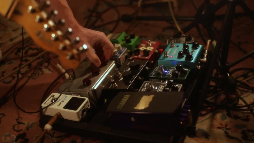 A man working with a guitar pedal board in a studio