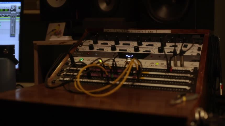 Analog synthesizer next to a computer screen indoors with speakers on the background