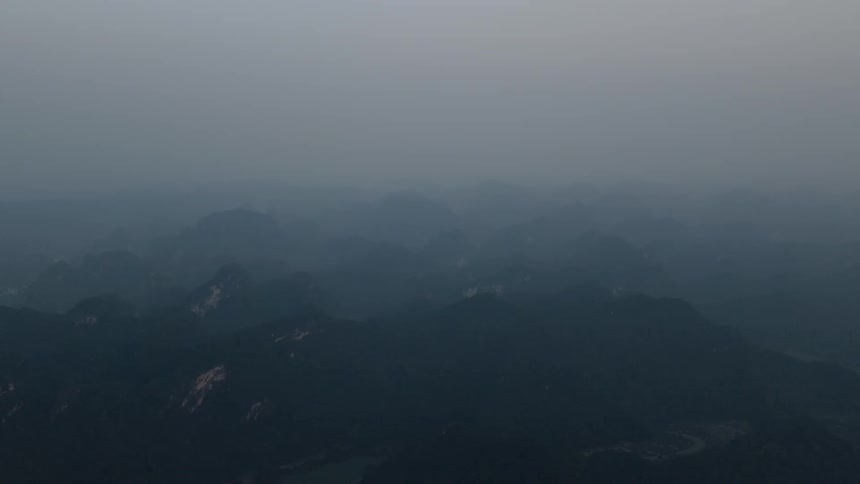 A view from above a dark mountain range under a thick layer of grey mist and fog during a dim and overcast day