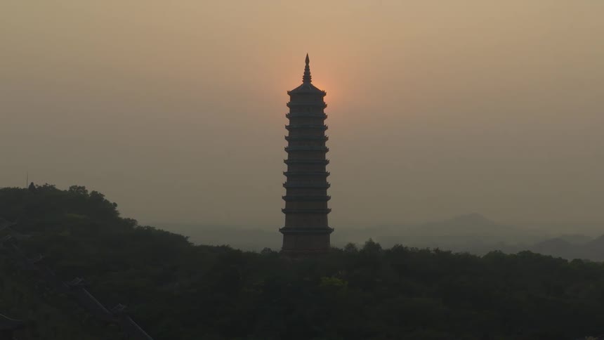 Asian pagoda tower stands tall in a hazy sky with the sun in the distance