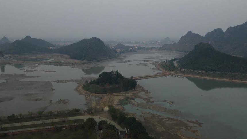 Light traffic travels along a highway near a network of bodies of water and mountains on a foggy day