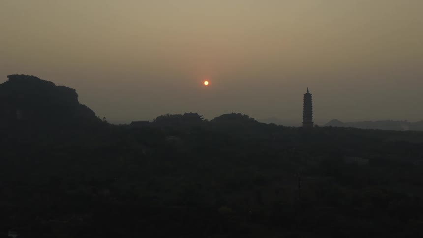 The sun is rising in the fog behind the lighthouse