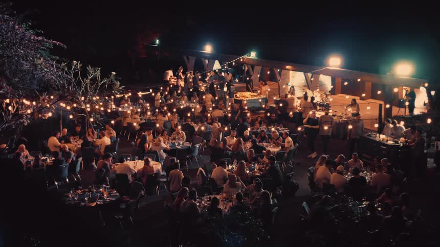 A large group of people are eating at outdoor tables at night