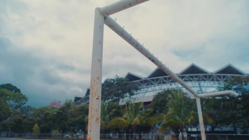 Metal structure with small hooks stands near a large building surrounded by palm trees on a cloudy day