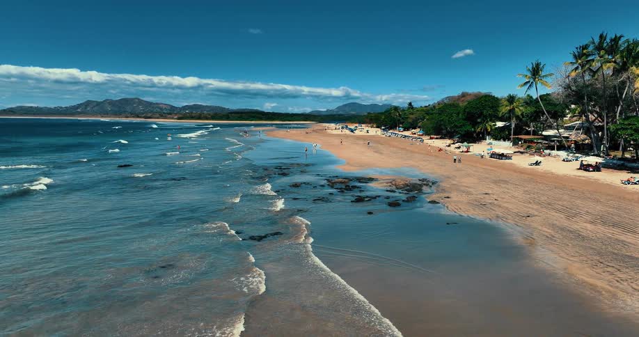 People enjoy the beach near resort buildings as haze covers the forested mountains on the horizon