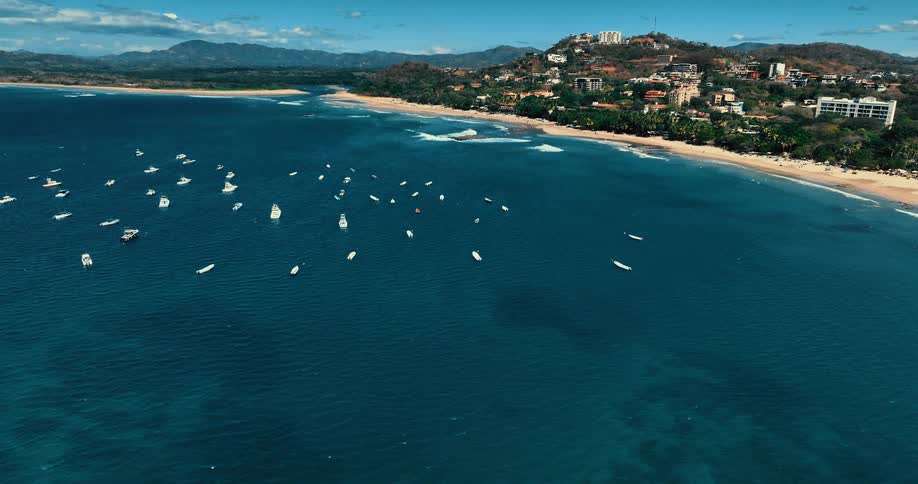 Several boats are anchored in the ocean water near a scenic beach
