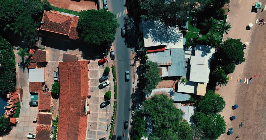 Aerial view of a neighborhood along the coast with cars in front of buildings on the streets and people walking on the beach