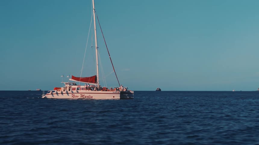 A sailboat sails on open ocean waters under blue skies