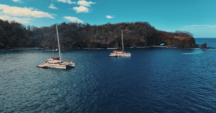 Two sailboats are docked in the ocean near an island at midday