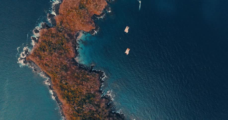 An island in the middle of the ocean as waves crash against the shoreline at midday