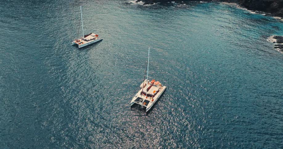 Two boats sailing on sparkling water off the mountain coast