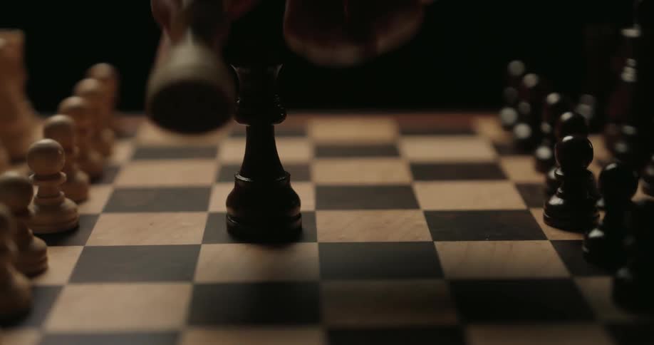 A close view shows a person moving a black queen chess piece to capture a white queen on a wooden board against a dark background