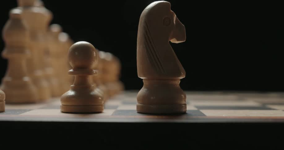 The video shows a closeup shot of wooden chess pieces arranged on a board against a dark background a knight is placed onto the board next to a pawn completing the formation with a deliberate and steady motion