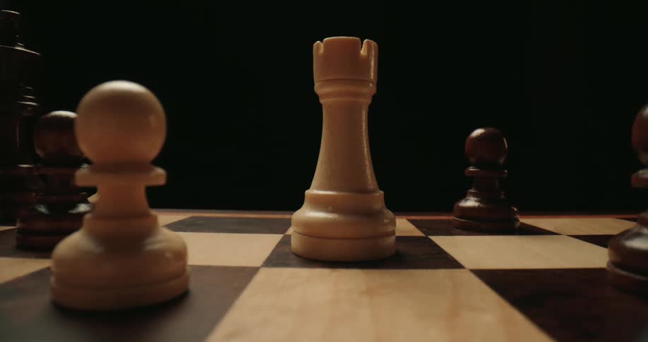 Human hand moving a chesspiece over a chessboard indoors