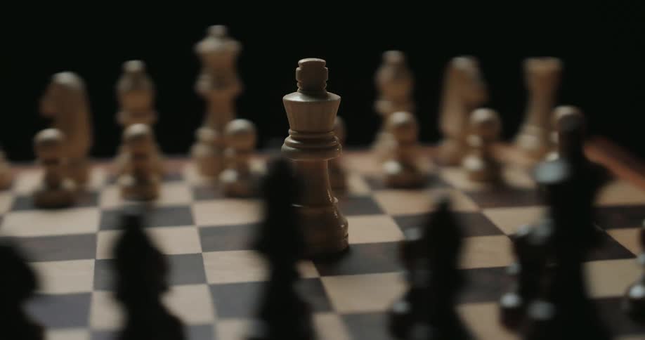 A close view shows a white wooden king chess piece standing in the center of a game board while the camera rotates around it in a circle against a dark background