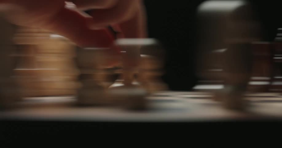 A close view shows a person moving a white pawn across a wooden chess board during a game against a dark background