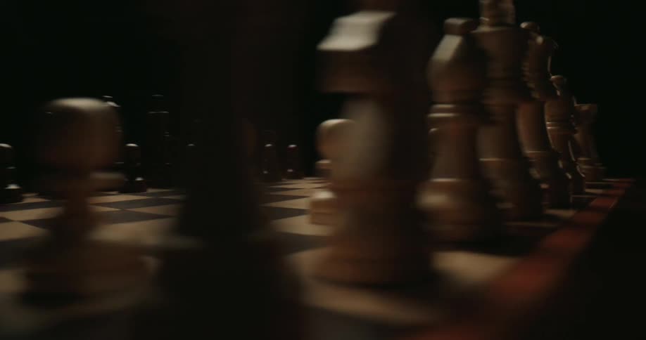 A chessboard with chess pieces is arranged for a game in dim lighting