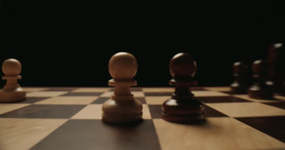 A lowangle camera glides smoothly across a wooden chessboard passing various stationary pieces before settling on a white pawn and a black pawn positioned facetoface against a dark moody background