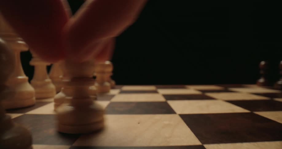 A hand moves a white pawn forward one square on a wooden chessboard against a dark background