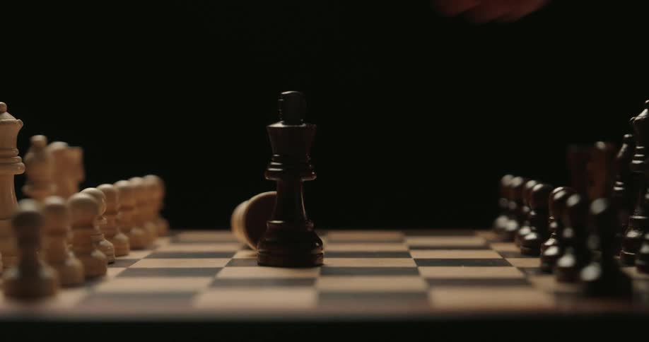A hand reaches into the frame to deliver a decisive checkmate knocking over the white king with a black king piece that then takes its place on the polished wooden chessboard amidst a dramatic and shadowy atmosphere