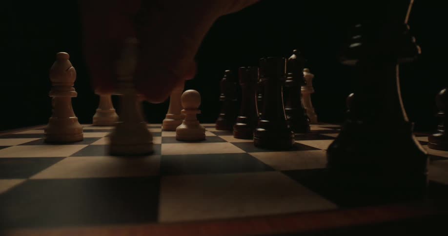 A hand repeatedly enters the frame from above to adjust or move various wooden chess pieces including bishops and pawns across the checkered boardthe camera maintains a lowangle cinematic perspective that emphasizes the height of the pieces against