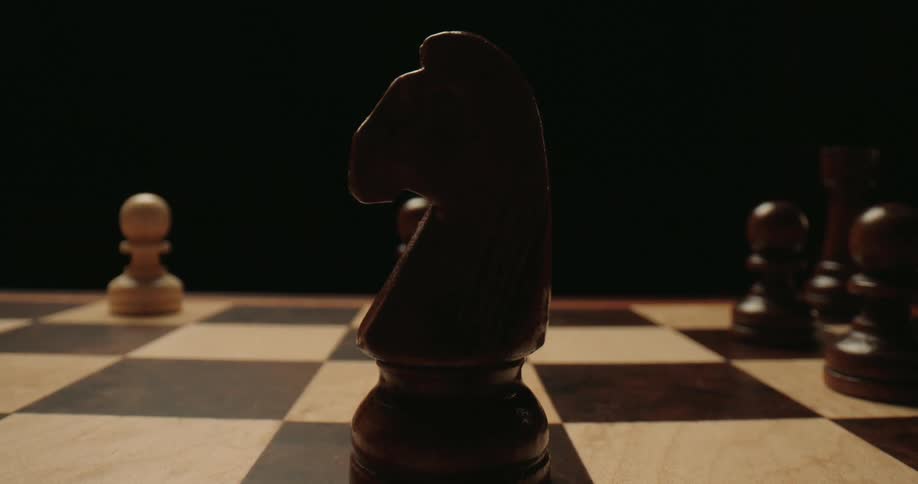 A hand places a dark knight chess piece on a chessboard