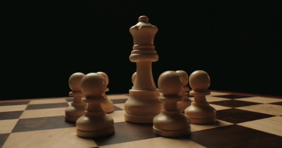 The video showcases a group of lightcolored wooden chess pieces positioned on a darktoned board a tall queen piece stands at the center surrounded by a tight formation of several pawns under dramatic highcontrast lighting