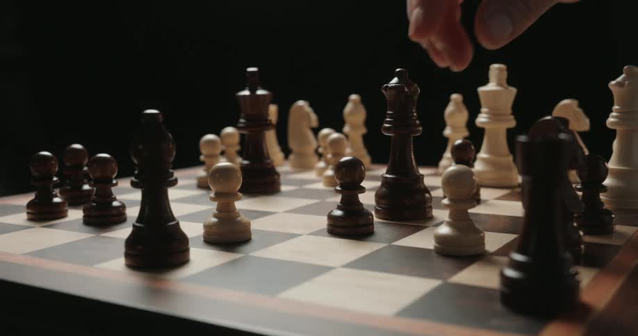 The video depicts a hand reaching into a chess game to move a white king across the board it then shows the hand moving a black queen to capture a nearby piece