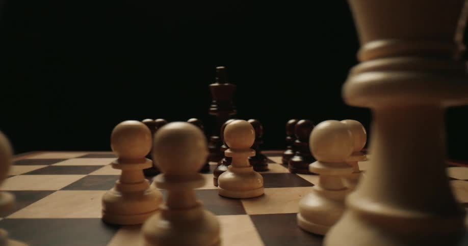Black and white chess pieces are arranged on a wooden board against a dark background