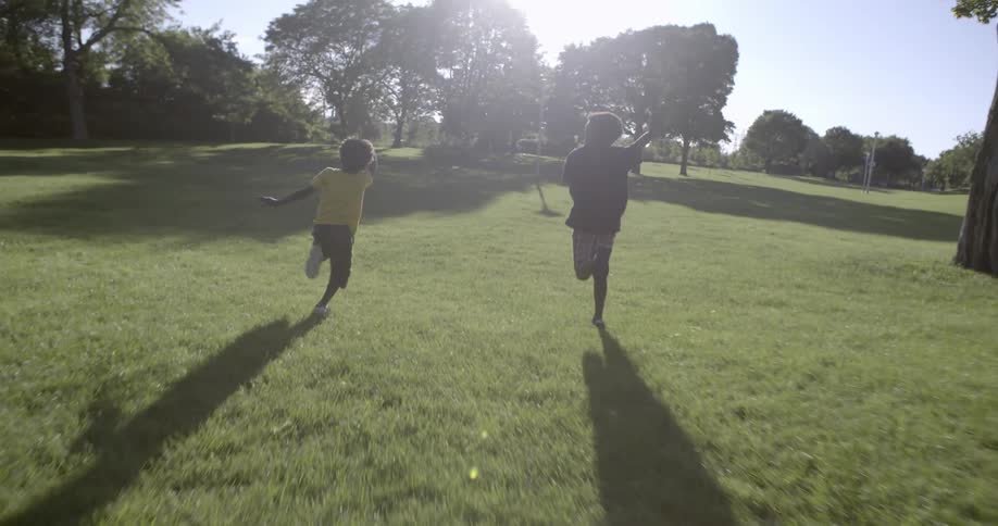 Two children run together on a green field