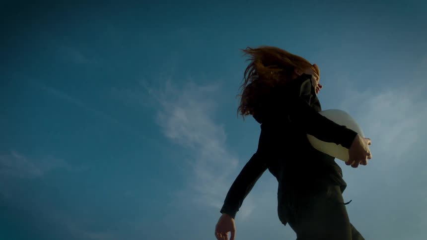A woman with red hair runs while carrying a white object under her arm