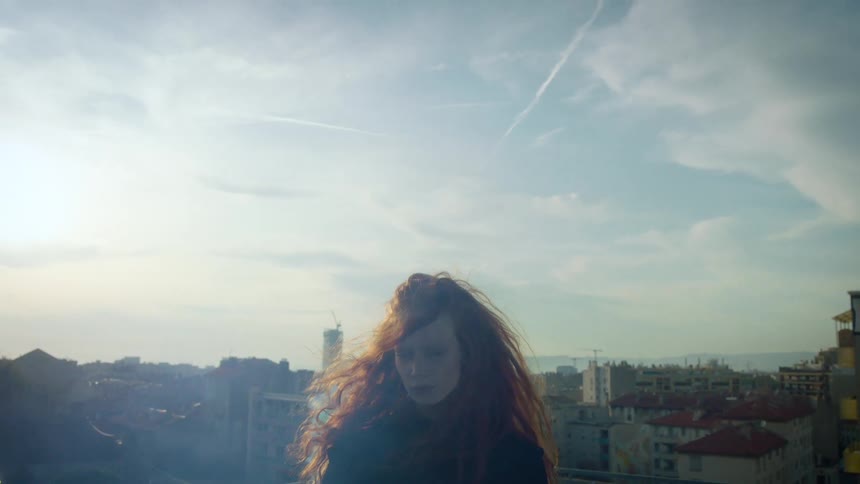 A woman stands on a building as smoke rises and the wind blows her hair