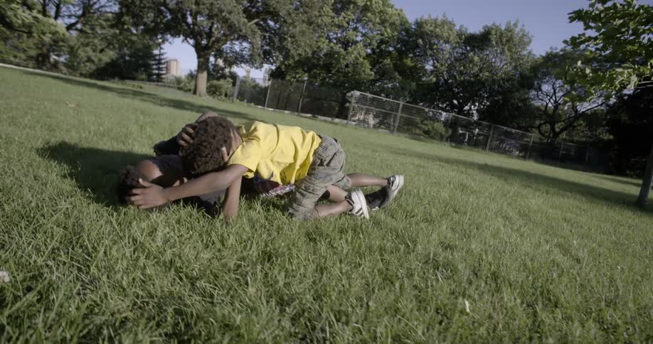 Two boys laugh as they wrestle in the grass