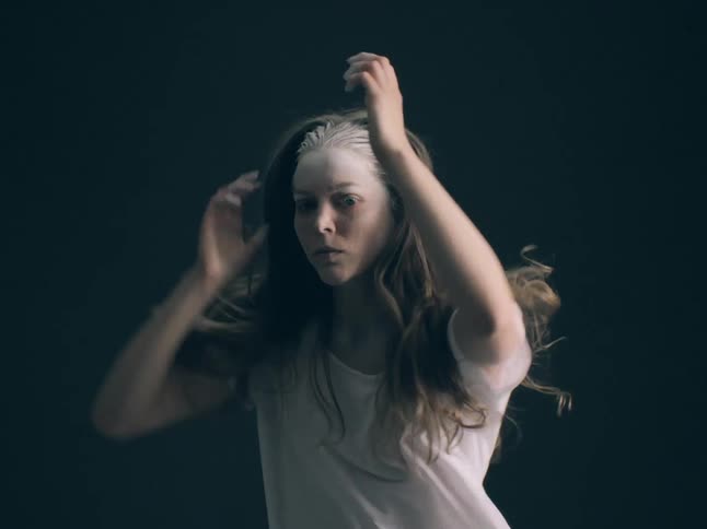 Young adult woman with white dusk sprinkled over her forehead dancing indoors in a room with flashing lights
