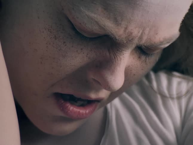 A young woman looking sad as she closes her eyes her face turned downward