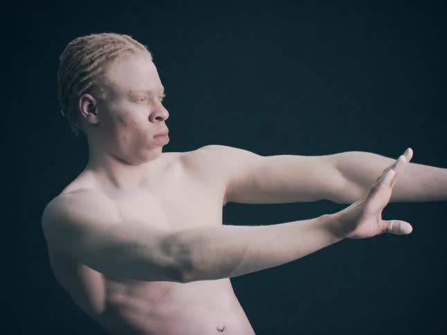 Shirtless albino black man doing a gesture with his arms indoors