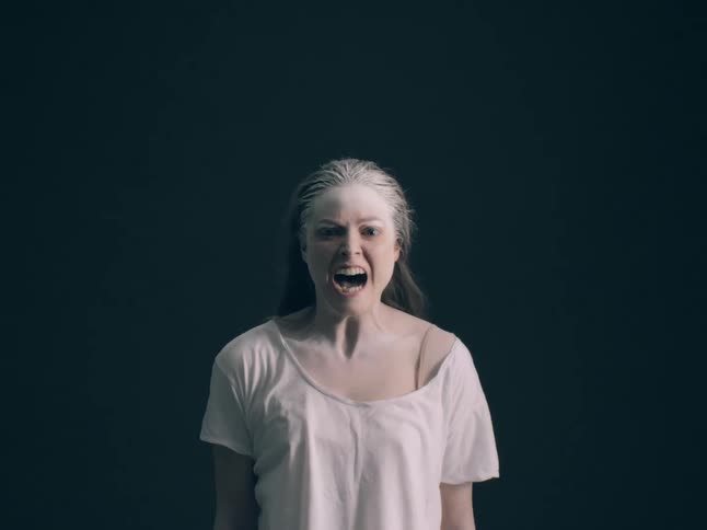 A woman with white powder on her face and hair screams against a dark background