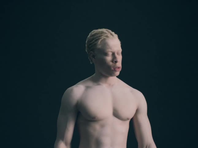 A close view shows a person with short blonde hair and white powder on their face as they move their head and arms quickly against a dark background