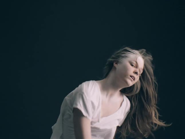 A woman with white powder in her hair performs an expressive dance in a dark studio