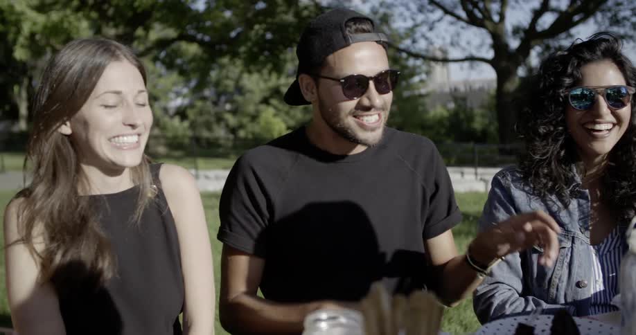 Man and two women smile and laugh outside at a picnic