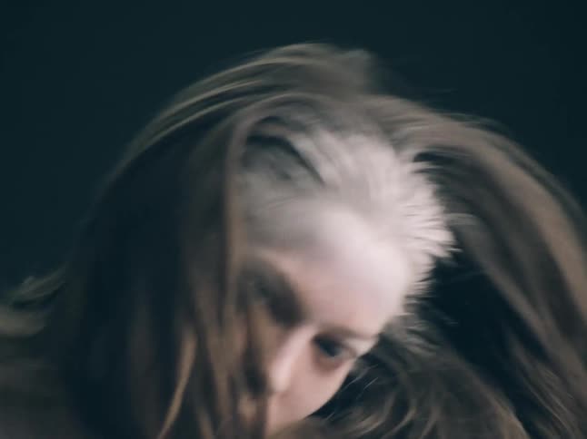 A woman with blonde hair jumps up and down in slow motion against a dark background