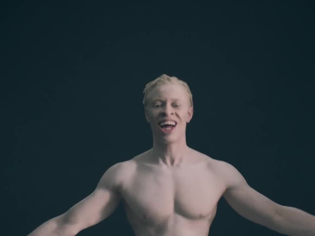 Albino black man hopping and stretching his arms while smiling indoors