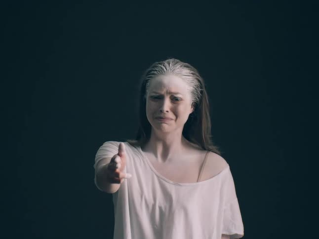A young woman wearing a white tshirt stands in sadness as she raises her hands