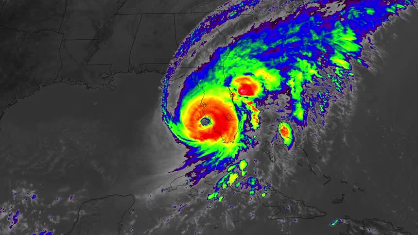 A thermal satellite view shows a large hurricane with a bright red and yellow eye moving over the coast and land with extensive purple and blue cloud structures spreading across the region