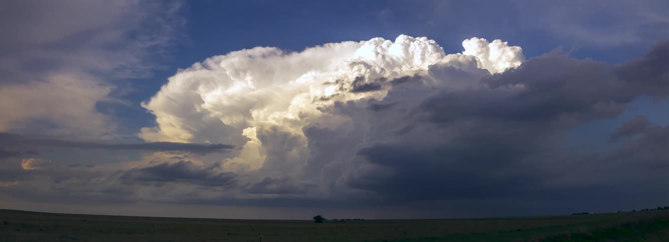Sunlight shines on white clouds over the rural landscape as dark clouds move across the sky